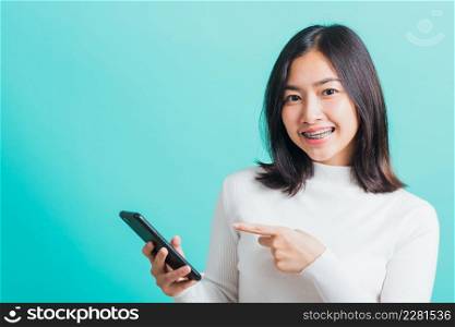 Portrait of Asian woman smile she holding and typing text message on a smartphone, female excited cheerful her reading mobile phone some social media isolated on a blue background, Technology concept