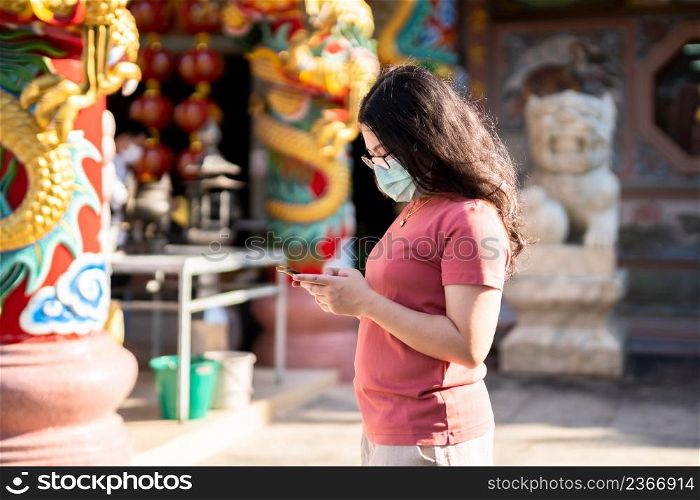 Portrait of asian woman traveler wear protective mask germs is looking up information on smartphone at Chinese buddhist temple or shrine,Prevention of the spread of COVID-19 virus,Chinese New Year