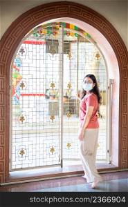 Portrait of asian woman traveler wear protective mask germs is praying at Chinese buddhist temple or shrine in Thailand,Prevention of the spread of COVID-19 virus,Chinese New Year