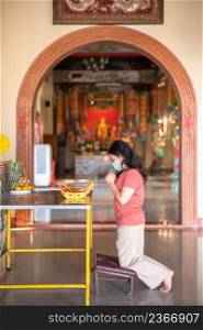 Portrait of asian woman traveler wear protective mask germs is praying at Chinese buddhist temple or shrine in Thailand,Prevention of the spread of COVID-19 virus,Chinese New Year
