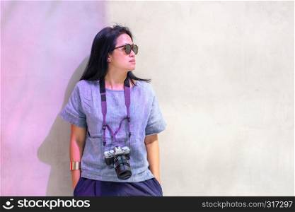 portrait of asian woman wear sunglasses with camera leaning at concrete wall with sunshade in day light.fashion traveler.