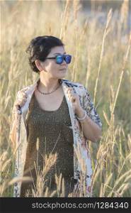 portrait of asian woman wearing sun glasses standing with relaxing post in beautiful grass field