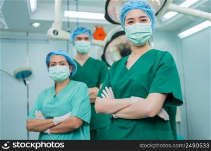 Portrait of Asian women surgeon and nurse with medical mask standing with arms crossed in operation theater at a hospital. Team of Professional surgeons. Healthcare, emergency medical service concept