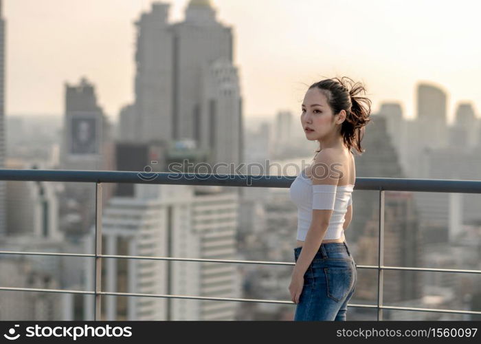 Portrait of Asian Yong woman in sexy fashion suit standing on the rooftop over the cityscape background, beautiful shape of body concept