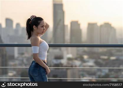 Portrait of Asian Yong woman in sexy fashion suit standing on the rooftop over the cityscape background, beautiful shape of body concept