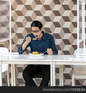 Portrait of asian young adult man eat fried rice food at new normal social distance restaurant with table shiled partition. Restaurant new normal lifestyle and food concept.