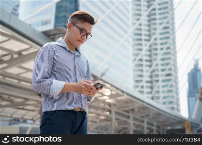 Portrait of asian young businessman standing at Outside Office. Young businessman wear suit smiling and looking at smartphone