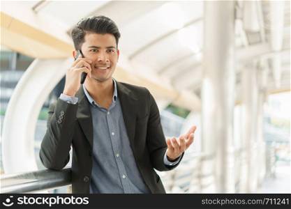 Portrait of asian young businessman standing at Outside Office. A man wear suit so smart and talking on smartphone to business conversation.