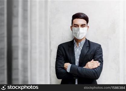 Portrait of Asian Young Businessman Wearing Surgical Mask and standing at the Wall, Smiling and Crossed Arms, Looking at camera