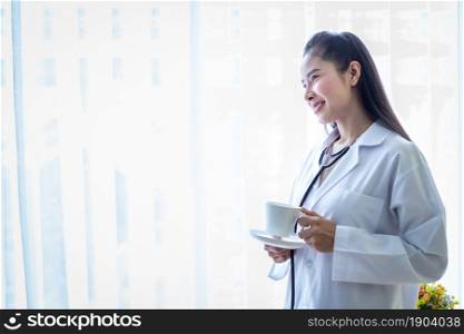 Portrait of asian young female doctor eating coffee from a cup and stethoscope with in hospital background.