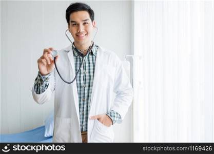 Portrait of Asian Young man doctor therapeutic advising smiling face abstract blur with focus show holding stethoscope with in hospital background.