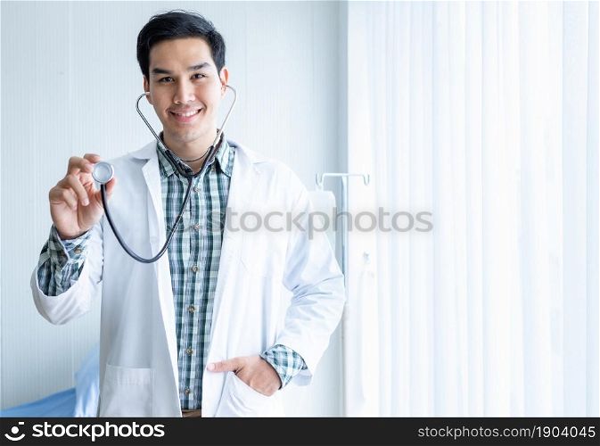 Portrait of Asian Young man doctor therapeutic advising smiling face abstract blur with focus show holding stethoscope with in hospital background.