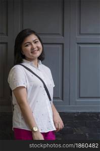 Portrait of Asian young smiling woman in casual clothing standing on vintage wall outside of coffee shop in vertical frame