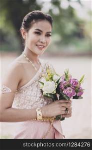 portrait of asian younger woman wearing thai tradition clothes holding pink lotus flower in hand toothy smiling face