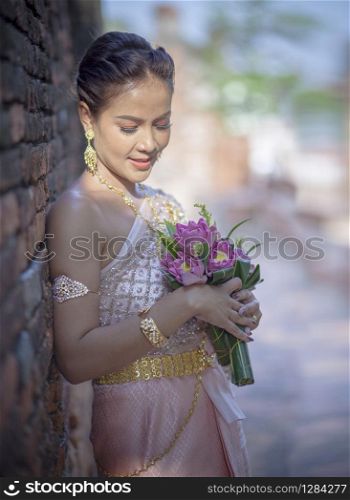 portrait of asian younger woman wearing thai tradition clothes holding pink lotus flower in hand toothy smiling face