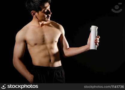 portrait of athletic muscular bodybuilder man with naked torso six pack abs holding protein drink. fitness workout concept