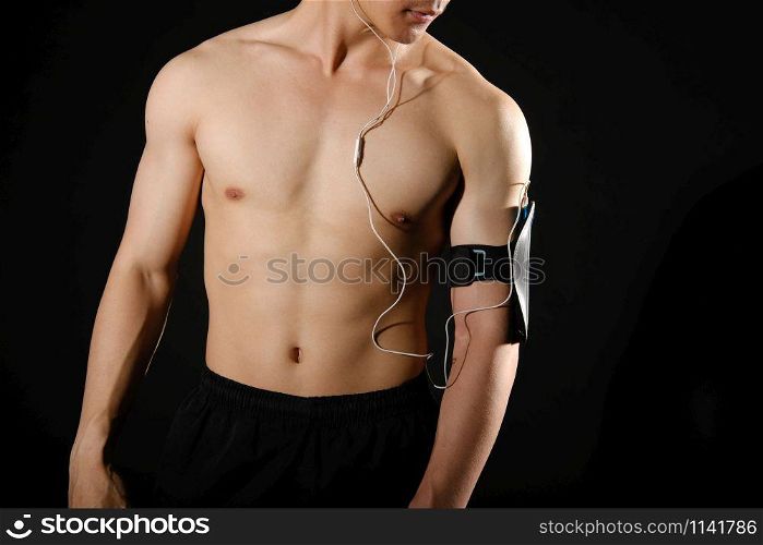 portrait of athletic muscular bodybuilder man with smart mobile phone armband listening to music. fitness workout concept