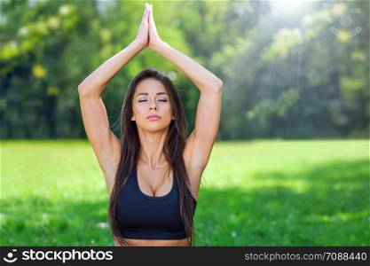 Portrait of attractive and young woman with close eyes doing outdoors yoga meditation in a park on a sunny day