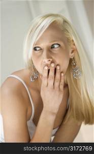 Portrait of attractive blonde Caucasian young adult woman covering mouth with hand in a surprised expression.