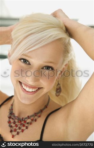 Portrait of attractive blonde Caucasian young adult woman holding up hair smiling and looking at viewer.