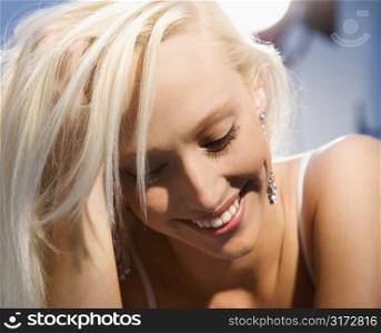 Portrait of attractive blonde Caucasian young adult woman smiling and looking down.