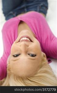 Portrait of attractive blonde Caucasian young adult woman wearing fuchsia lying upside down smiling and looking at viewer.