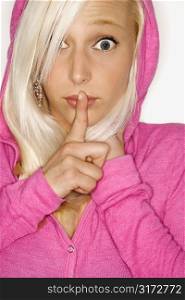 Portrait of attractive blonde Caucasian young adult woman wearing fuchsia with finger over mouth looking at viewer.