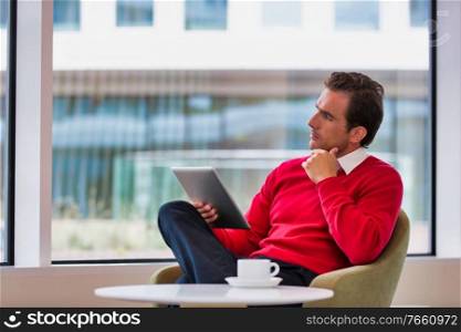 Portrait of attractive businessman using digital tablet while sitting and drinking coffee in lobby
