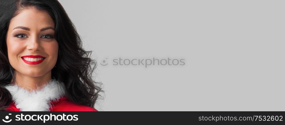 Portrait of attractive caucasian smiling woman brunette studio shot in santa&rsquo;s red dress copy space for text on gray background. Christmas woman portrait
