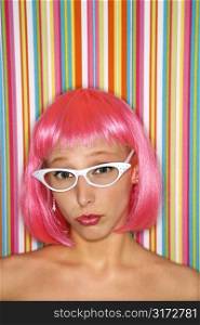 Portrait of attractive Caucasian young adult woman wearing pink wig against striped background looking at viewer.
