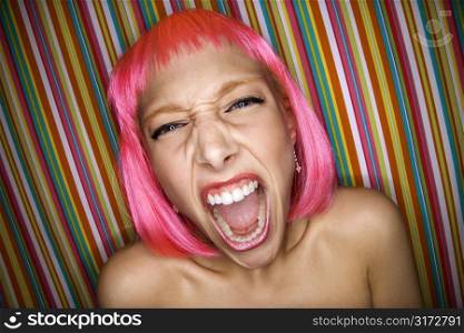 Portrait of attractive Caucasian young adult woman wearing pink wig against striped background making sassy expression at viewer.