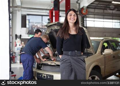Portrait of attractive female in garage while people working in background