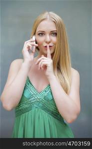 Portrait of attractive girl calling by phone with finger on lips. Concept of student show quiet, silence, secret gesture, young pretty blonde woman