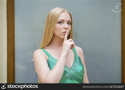 Portrait of attractive girl with finger on lips, concept of student show quiet, silence, secret gesture, young pretty blonde woman in green dress