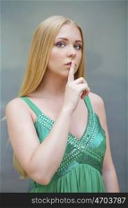 Portrait of attractive girl with finger on lips, concept of student show quiet, silence, secret gesture, young pretty blonde woman in green dress