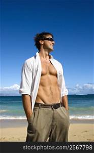 Portrait of attractive man standing with shirt unbuttoned wearing sunglasses on Maui, Hawaii beach.