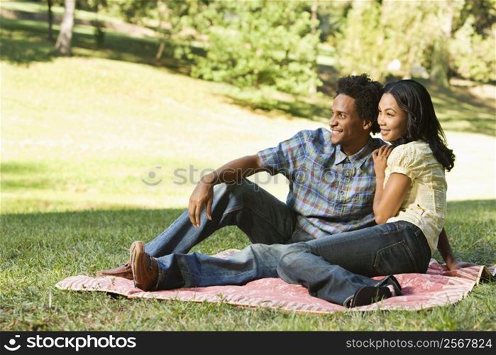 Portrait of attractive smiling couple in park sitting on picnic blanket.