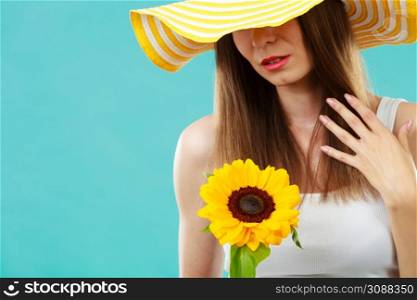 portrait of attractive summer woman in yellow hat with sunflower in hand on blue background