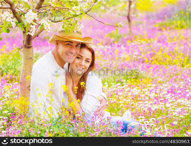 Portrait of attractive woman and handsome man sitting down on floral field, young lovers, having fun in the garden, romantic date, love concept