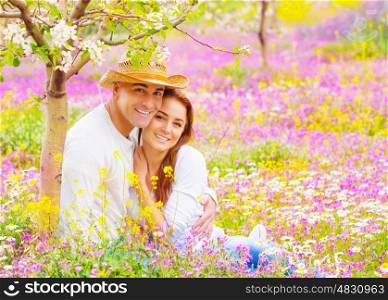 Portrait of attractive woman and handsome man sitting down on floral field, young lovers, having fun in the garden, romantic date, love concept