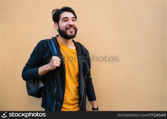Portrait of attractive young beared man with backpack on his shoulders against yellow background. Urban concept.