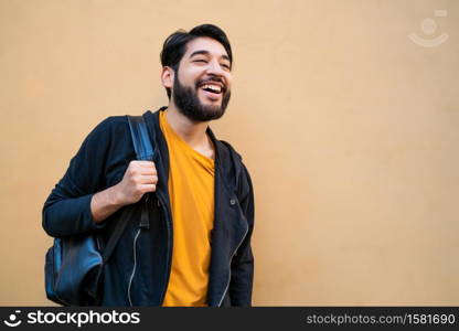 Portrait of attractive young beared man with backpack on his shoulders against yellow background. Urban concept.