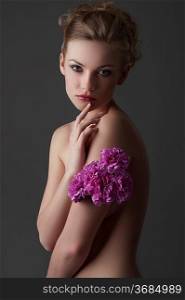 portrait of attractive young blond naked woman with some carnation purple flower around one arm