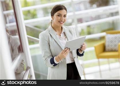 Portrait of attractive young business woman smiling confidently and working online with a digital tablet while standing in the modern office