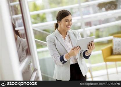 Portrait of attractive young business woman smiling confidently and working online with a digital tablet while standing in the modern office