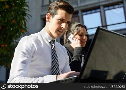 Portrait of attractive young businessman typing in a laptop computer in urban background
