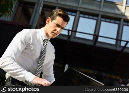 Portrait of attractive young businessman typing in a laptop computer in urban background
