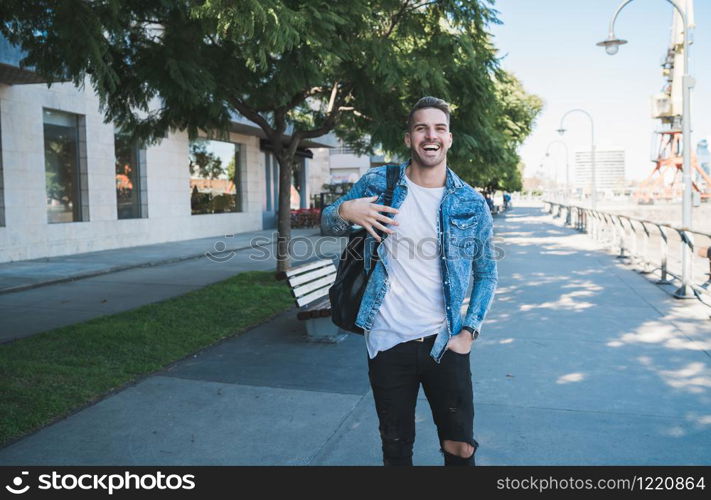 Portrait of attractive young man walking on the street with backpack on his shoulders. Urban concept.