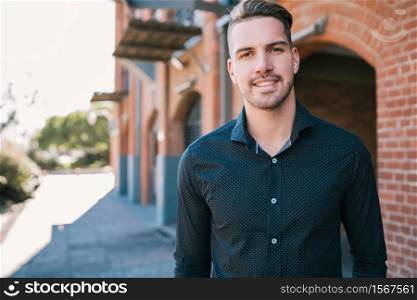 Portrait of attractive young man wearing casual clothes, standing outdoors with urban background.