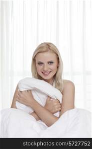 Portrait of attractive young woman holding bedsheet in bed